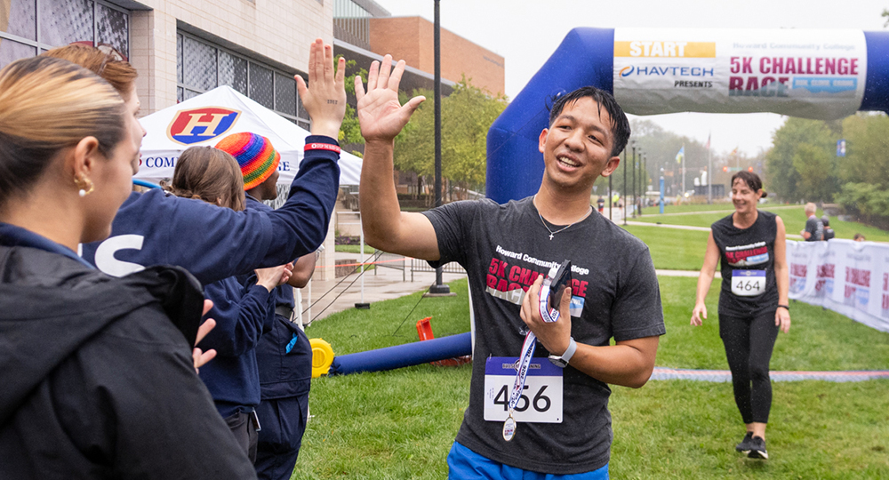 A runner crosses the finish line at the HCC 5k race and gives the spectators a high five. The race raises money for student scholarships.