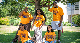 Five Dragon Days student ambassadors wearing yellow Dragon Days T-shirts smile and pose together on HCC's campus lawn.