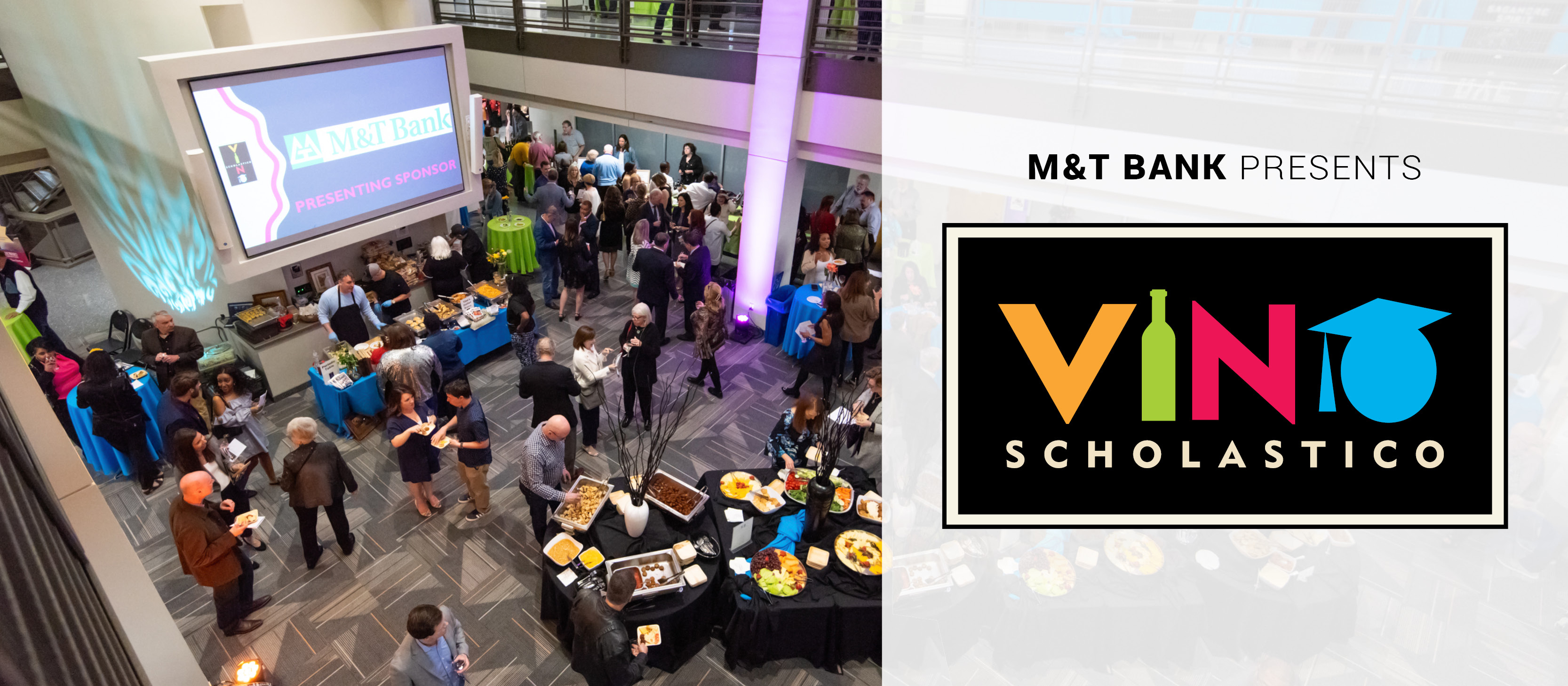 Crowd of people attending Vino Scholastico, a food and wine tasting event presented by M&T Bank, held in a modern indoor venue with vendor tables and a large screen displaying the event name. Logo on the right reads 'Vino Scholastico' with colorful letters, a wine bottle as the 'I', and a graduation cap over the 'O'.