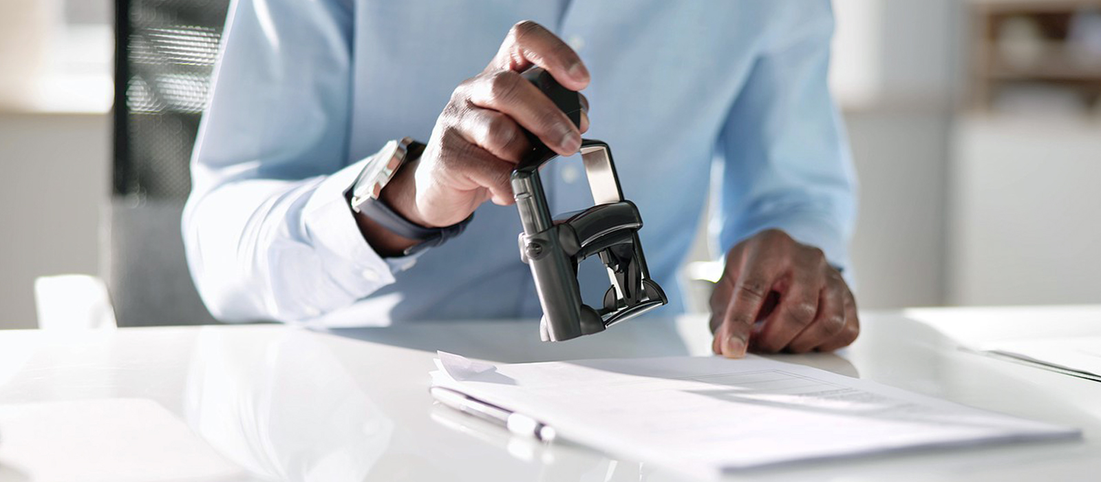 Close-up of a person in a light blue shirt using a stamp on an official document at a desk, symbolizing notary services.