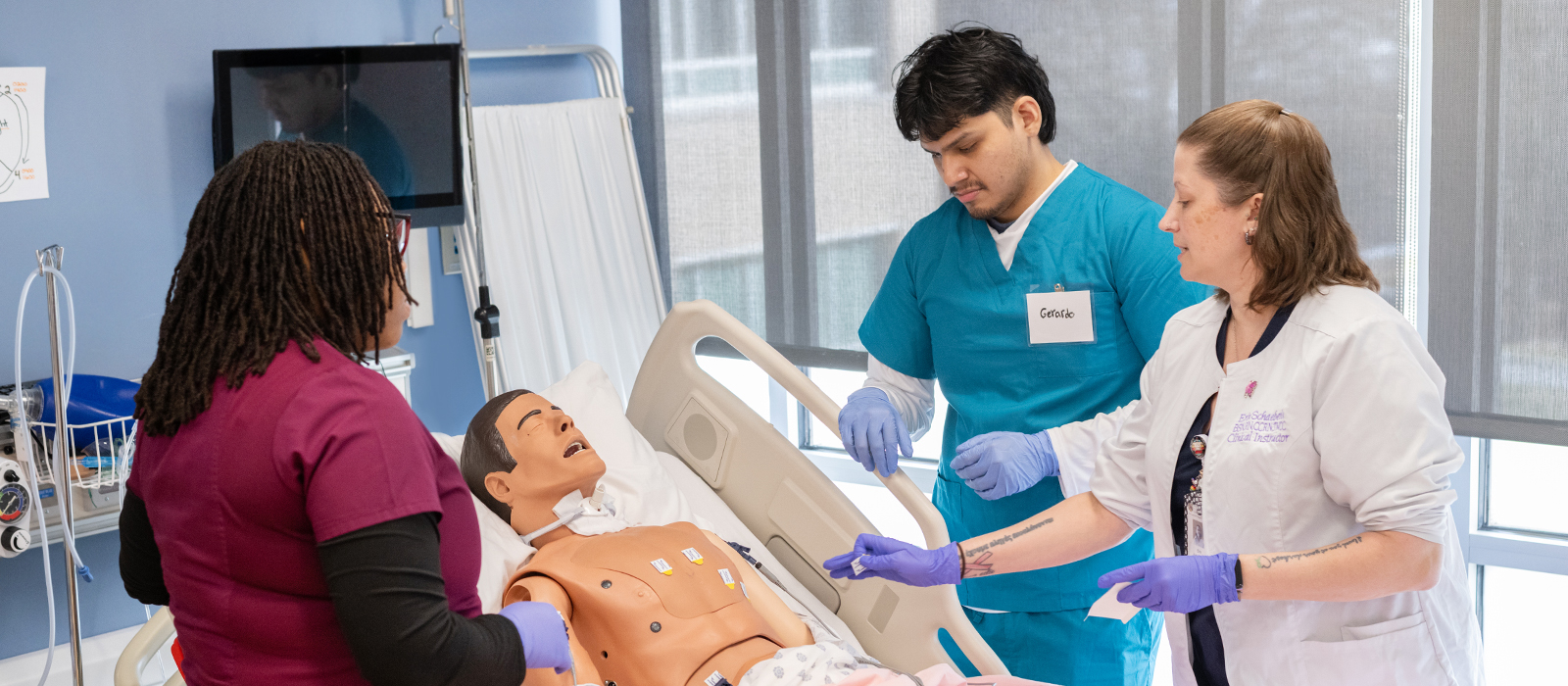 Patient Care Technician students practice clinical skills on a medical simulation mannequin under the guidance of an instructor in a hospital simulation lab.