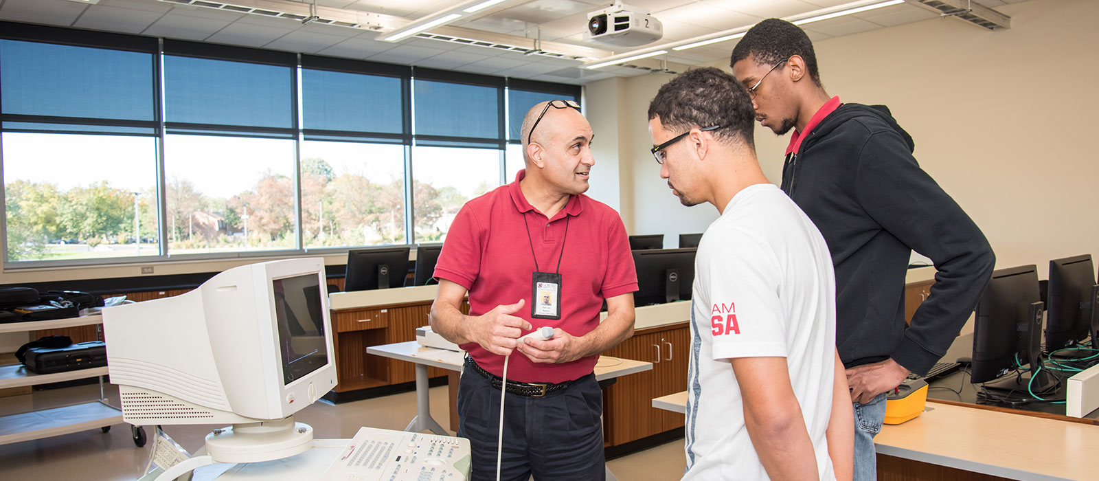 Two students and an instructor discussing a piece of biomedical equipment
