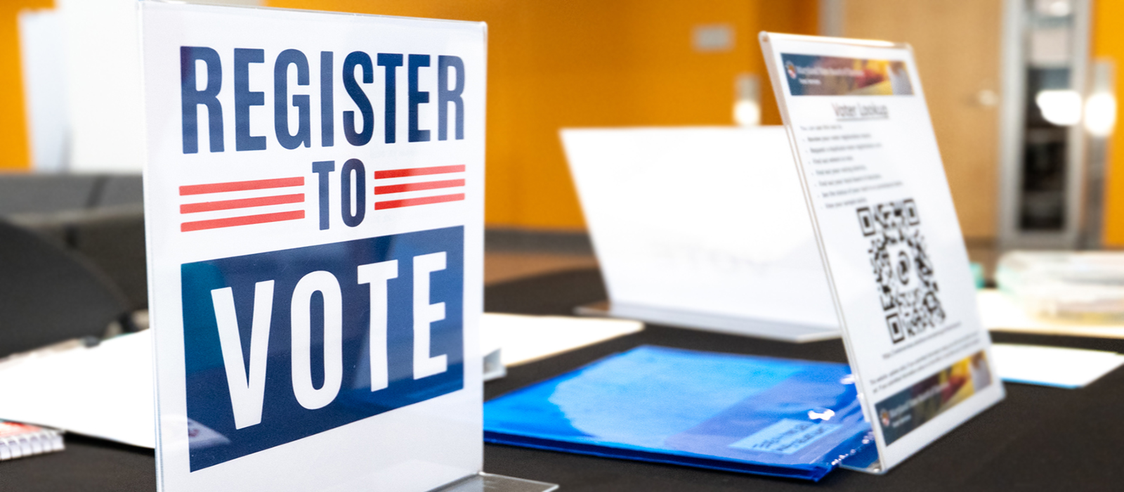 A voter registration table with a sign that says Register to Vote